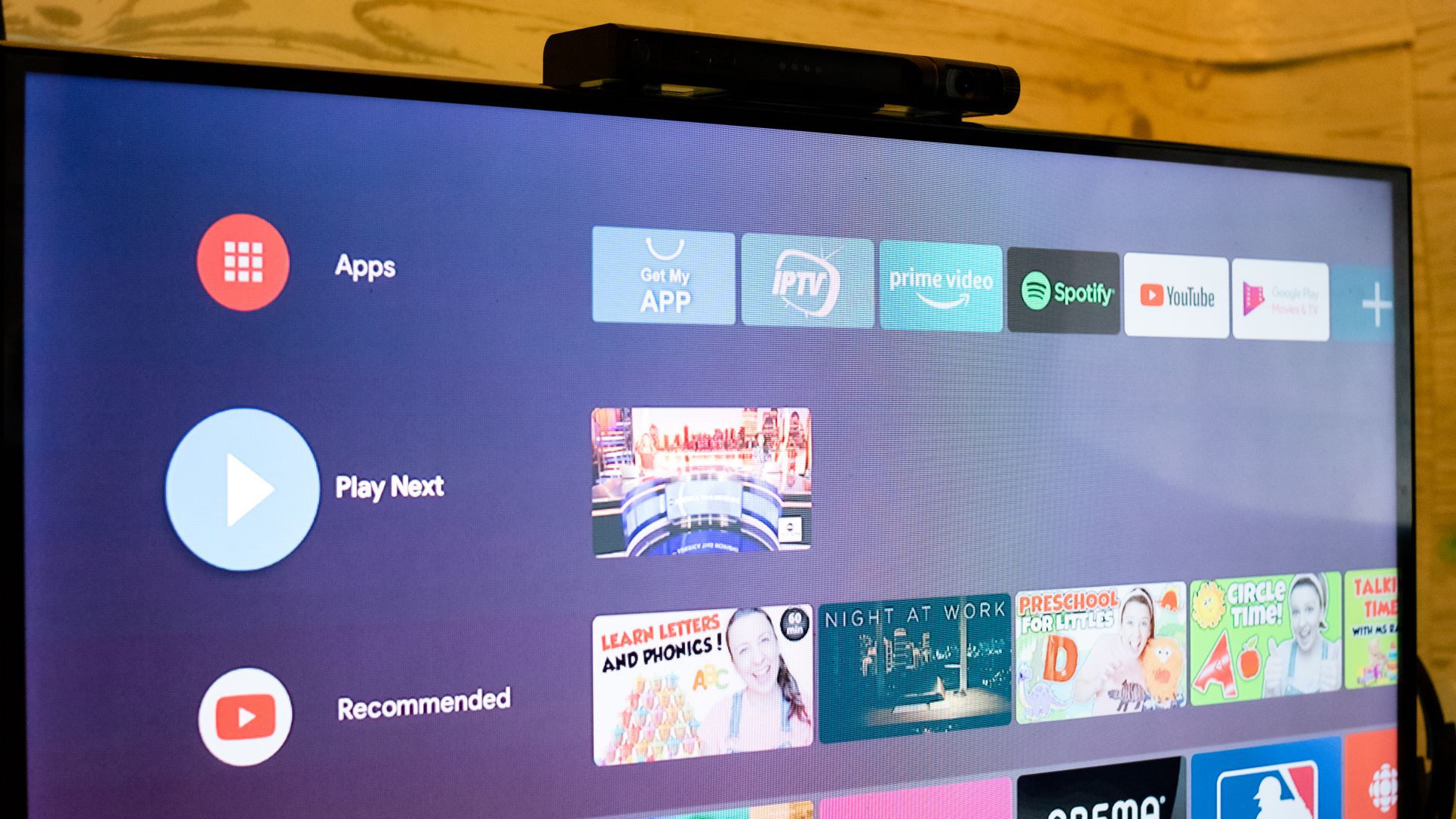 Mecool Now KA2 atop a smart TV showing its Android TV interface