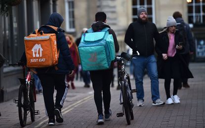 Just Eat and Deliveroo employees walking along a street together with their bicycles
