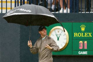 Rory McIlroy of Northern Ireland acknowledges the crowd as he walks onto the tee box underneath an umbrella as it rains on the 1st hole on Day Four of The 151st Open