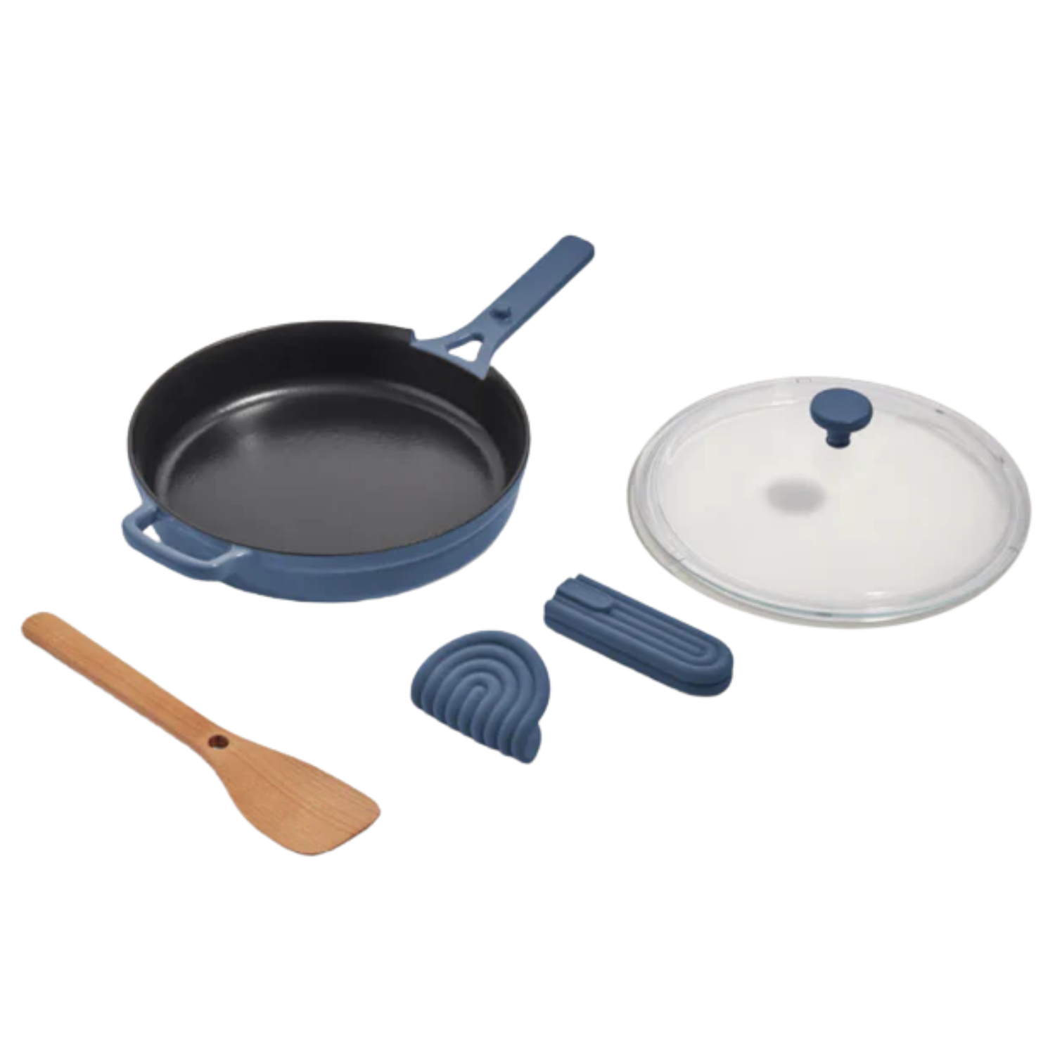 A cast iron pan with a deep blue exterior, a glass lid, heat protectant accessories and a wood spoon from Our Place
