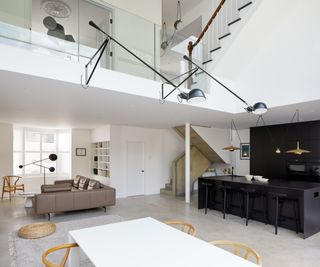 double height open plan living room with mezzanine level, glass balustrade and large wall lights extending into living space