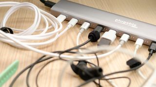 Plugable PS-10CC 10-port USB-C charging hub in use on a wood desk with a range of accessories plugged in including earbuds, smartwatches and a digital camera