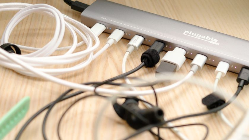 Plugable PS-10CC 10-port USB-C charging hub in use on a wood desk with a range of accessories plugged in including earbuds, smartwatches and a digital camera