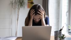 Frustrated unhappy laptop user girl touching head at work table with computer