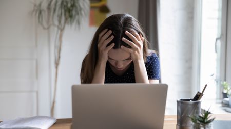 Frustrated unhappy laptop user girl touching head at work table with computer