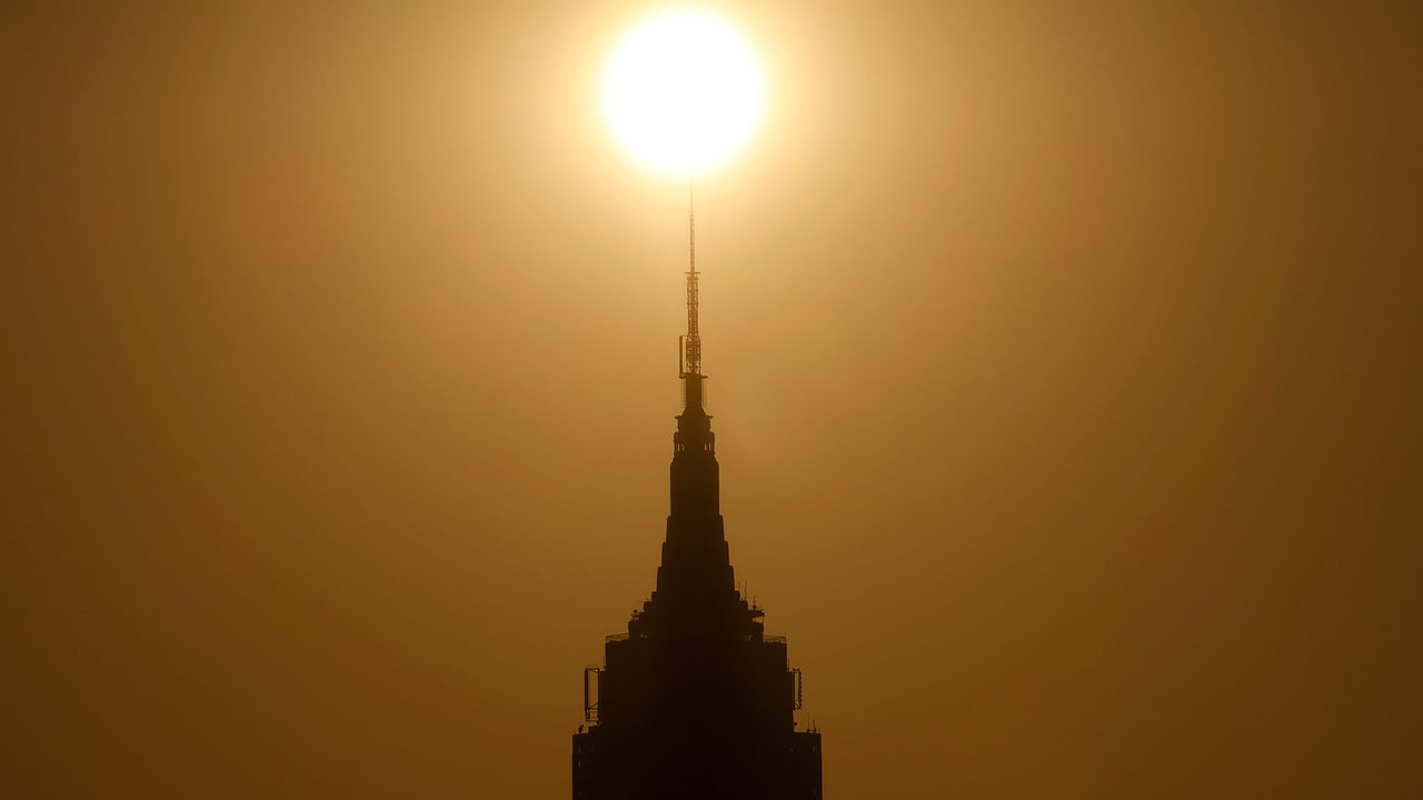 A silhouette of the Empire State Building is seen under a brown, glowing, smoggy sky.