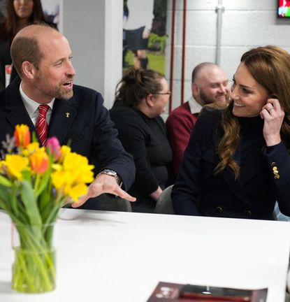 Prince William and Kate Middleton sitting at a white table smiling at each other during the Six Nations Rugby game