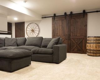 Industrial farmhouse style basement with sliding barn doors, wagon wheel on wall, and comfy sofa with footstool.