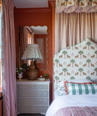 Pink bedroom with patterned bed canopy, printed headboard and bedside table with fabric patterned lampshade