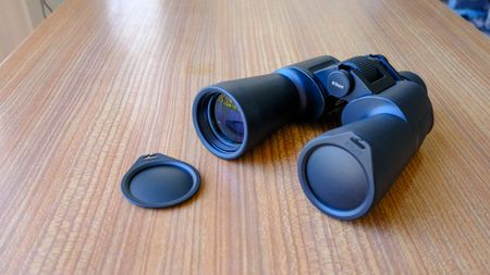 The Nikon Action 7x50 binoculars on a wooden table, with one lens cap on and one lens cap on the table. 