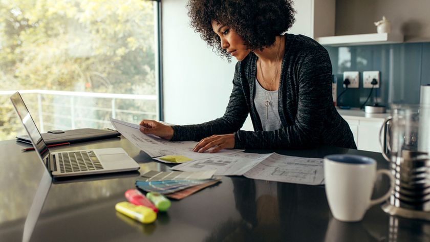 Woman looking at building plans on kitchen worktop with laptop and mug