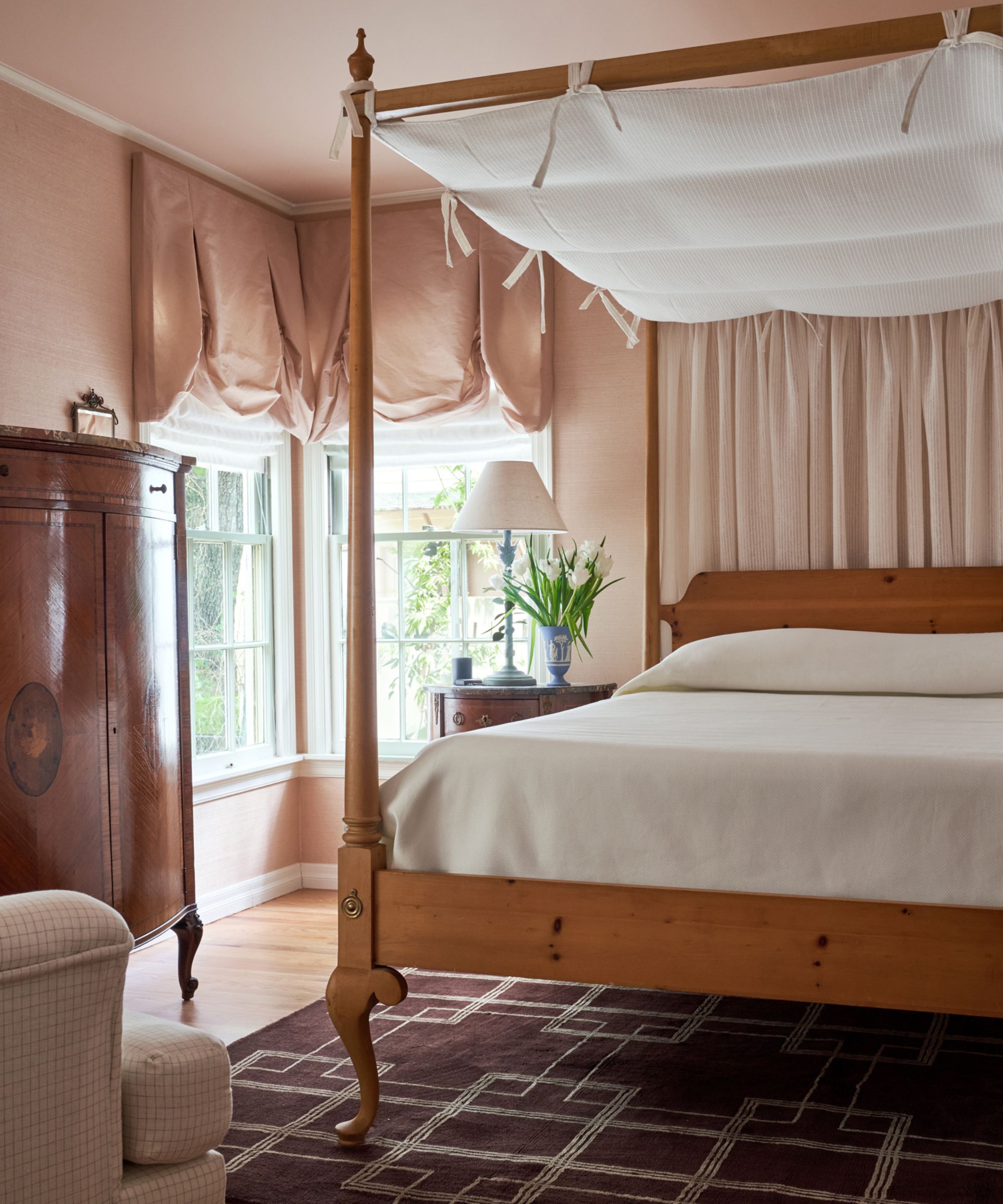 a peach pink primary bedroom with painted ceiling and wooden bed with linen canopy
