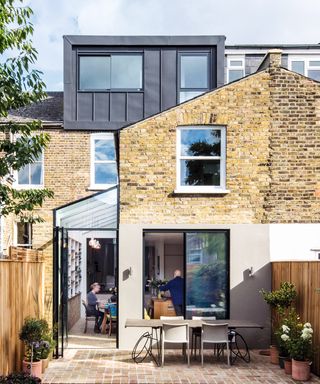 terraced house with small house extension at the side and box dormer, with people inside eating at dining table