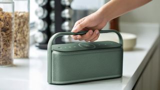 Anker Soundcore X600 in Aurora Green, on a kitchen table, being held by the handle