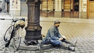 Lunch of a French soldier in front of a damaged library. 1st April 1917. He is sitting at a lamp post in a square in Reims with his bicycle next to him. Western Front. World War I. Autochrome Lumière. Photo: Paul Castelnau (1880-1944). France. (Photo by Galerie Bilderwelt/Getty Images)