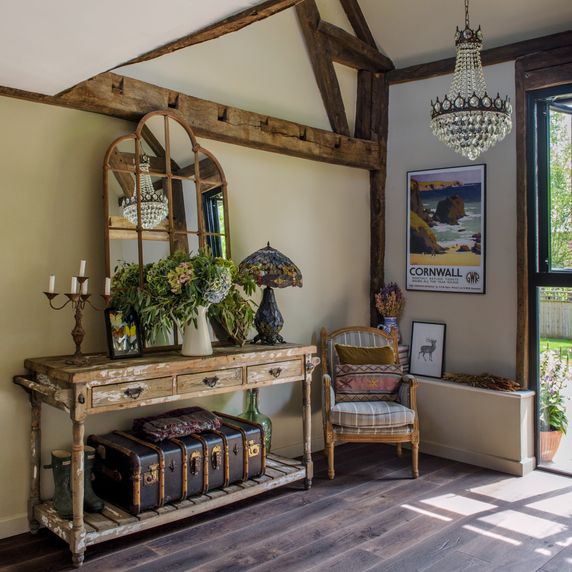 A large hallway with an antique console table with a stained glass table lamp, a candelabra and a window-style mirror