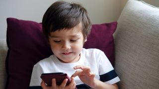 Dark-haired boy of about 5 using smarthphone while sitting on sofa.