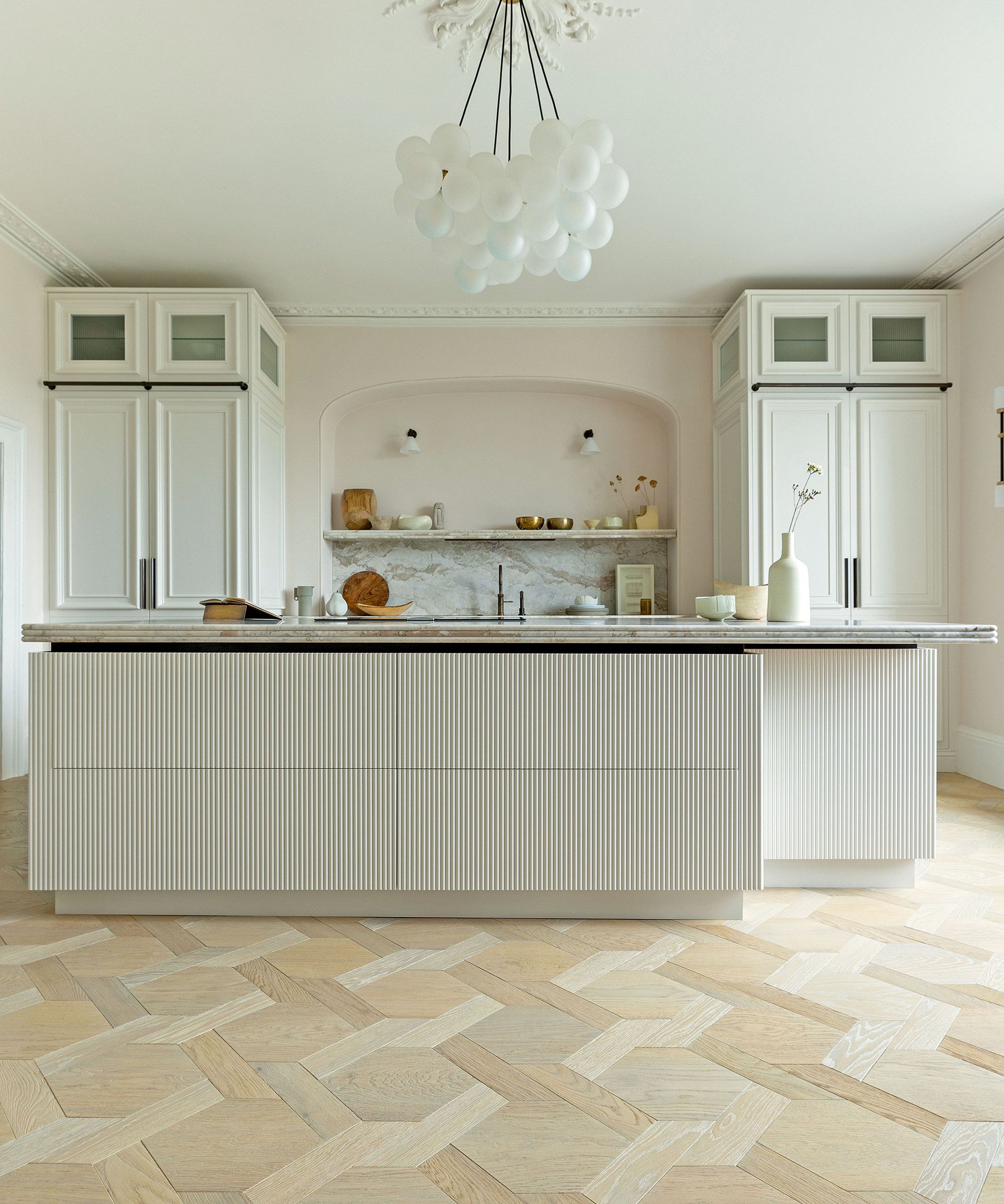 White kitchen with cream cabinets and fluted island and parquet floor
