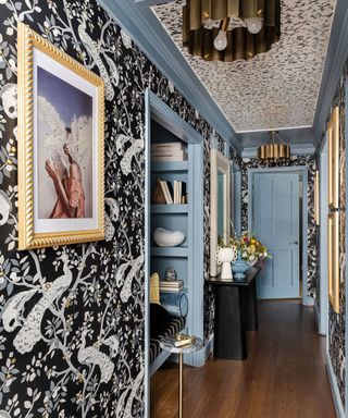 A light blue entryway with black and white wallpaper, gold antique framed art and a seating nook