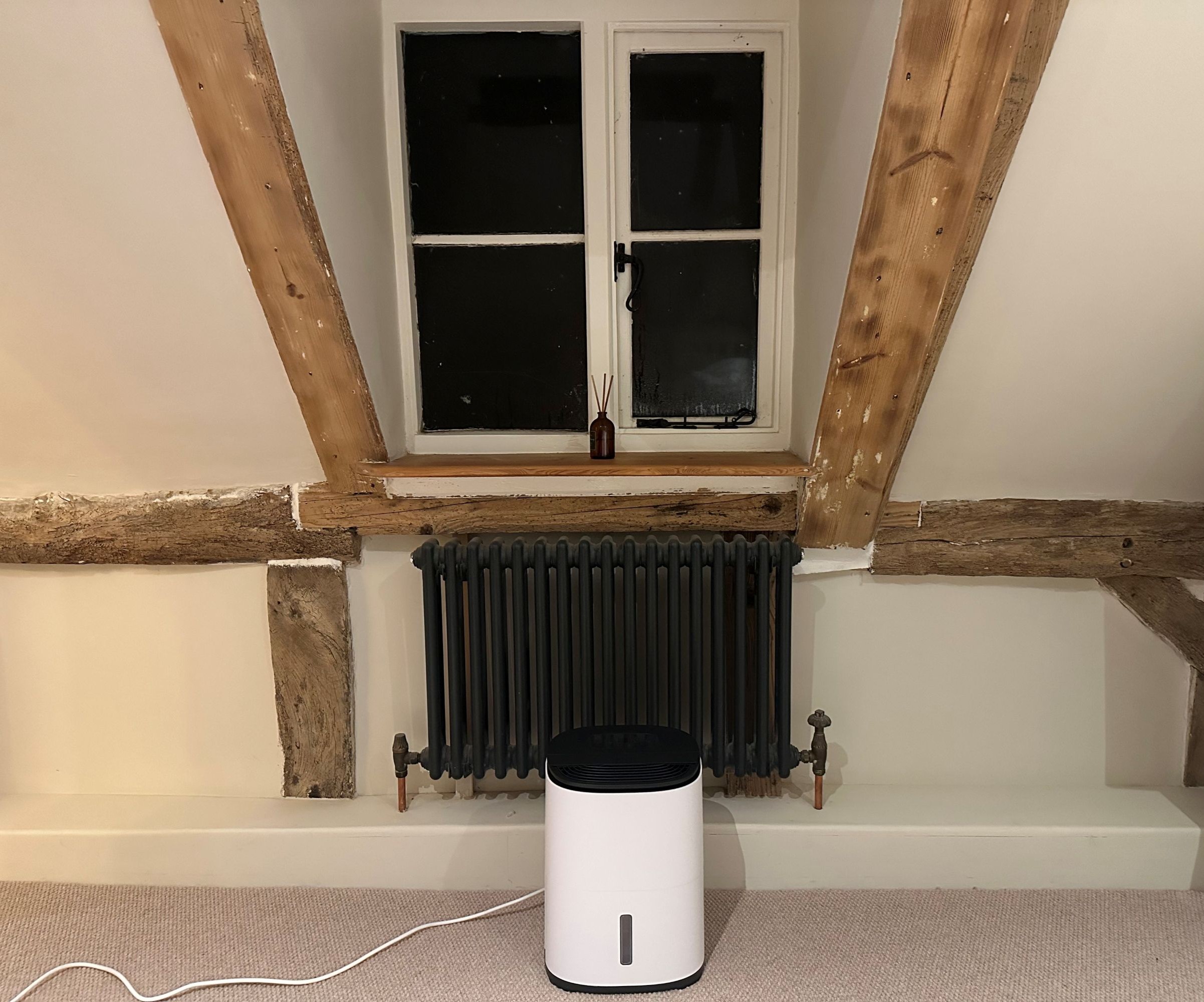The small dehumidifier in a bedroom with cream coloured carpet and oak beams