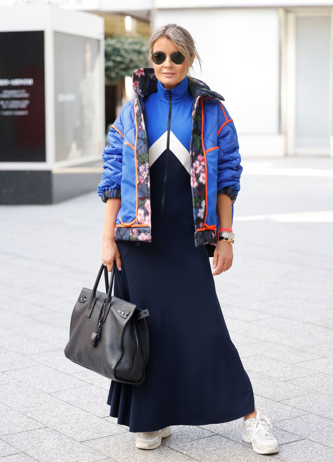 Influencer Gitta Banko wearing a blue tracksuit maxi dress by Victoria Beckham, a multicolored floral print reversible jacket by Konrad, a black bag by Saint Laurent, sunglasses by Ray-Ban and white sneaker by Chanel, all by loui.rocks during a street style shooting on October 17, 2022 in Dusseldorf, Germany.