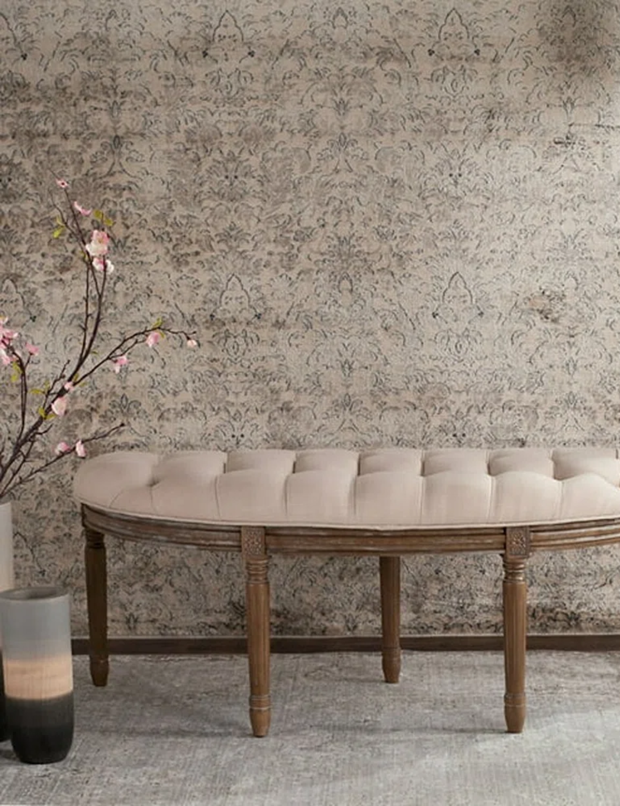 Button-tufted entryway bench with weathered wooden legs pictured inside of a patterned entryway area.