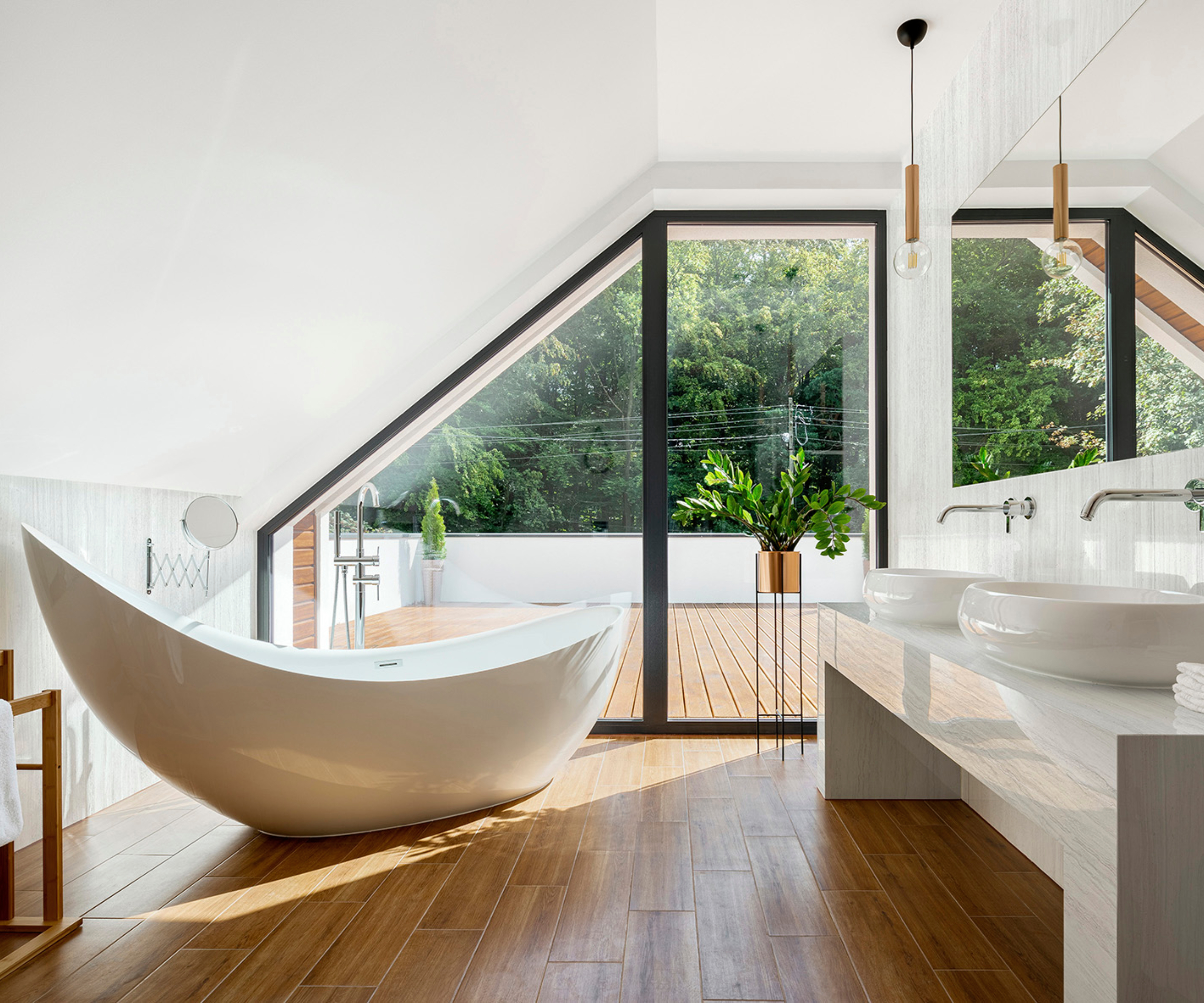 bathroom with sloped ceiling, curved white freestanding bath, window and door leading onto roof terrace, white large vanity unit with double sinks
