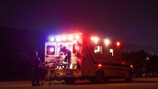 An ambulance parked at night in the US, with two paramedics wheeling a patient in.