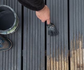 Hands painting faded old garden wooden decking with grey paint