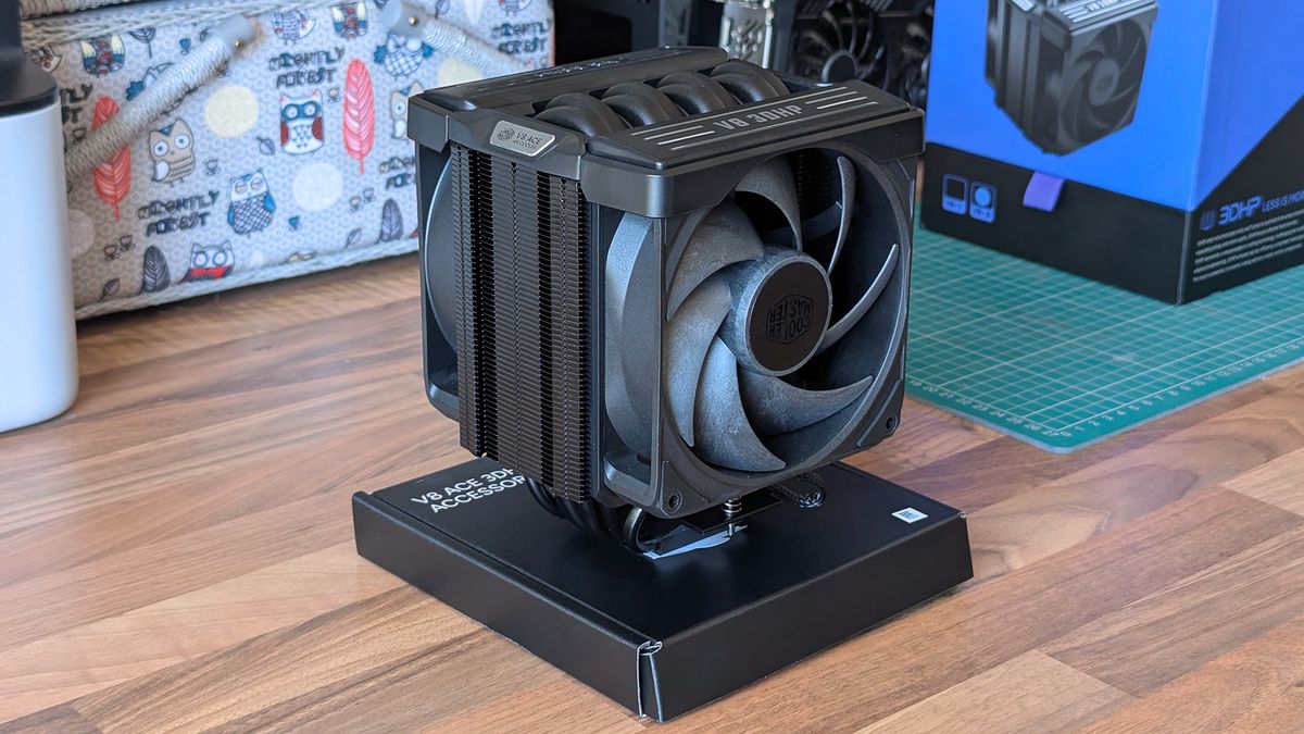 The Cooler Master V8 ACE 3DHP CPU cooler sits on a wooden desk, displaying its dual‑fan layout, heat pipe array, and black shroud with &ldquo;V8 3DHP&rdquo; labeling.