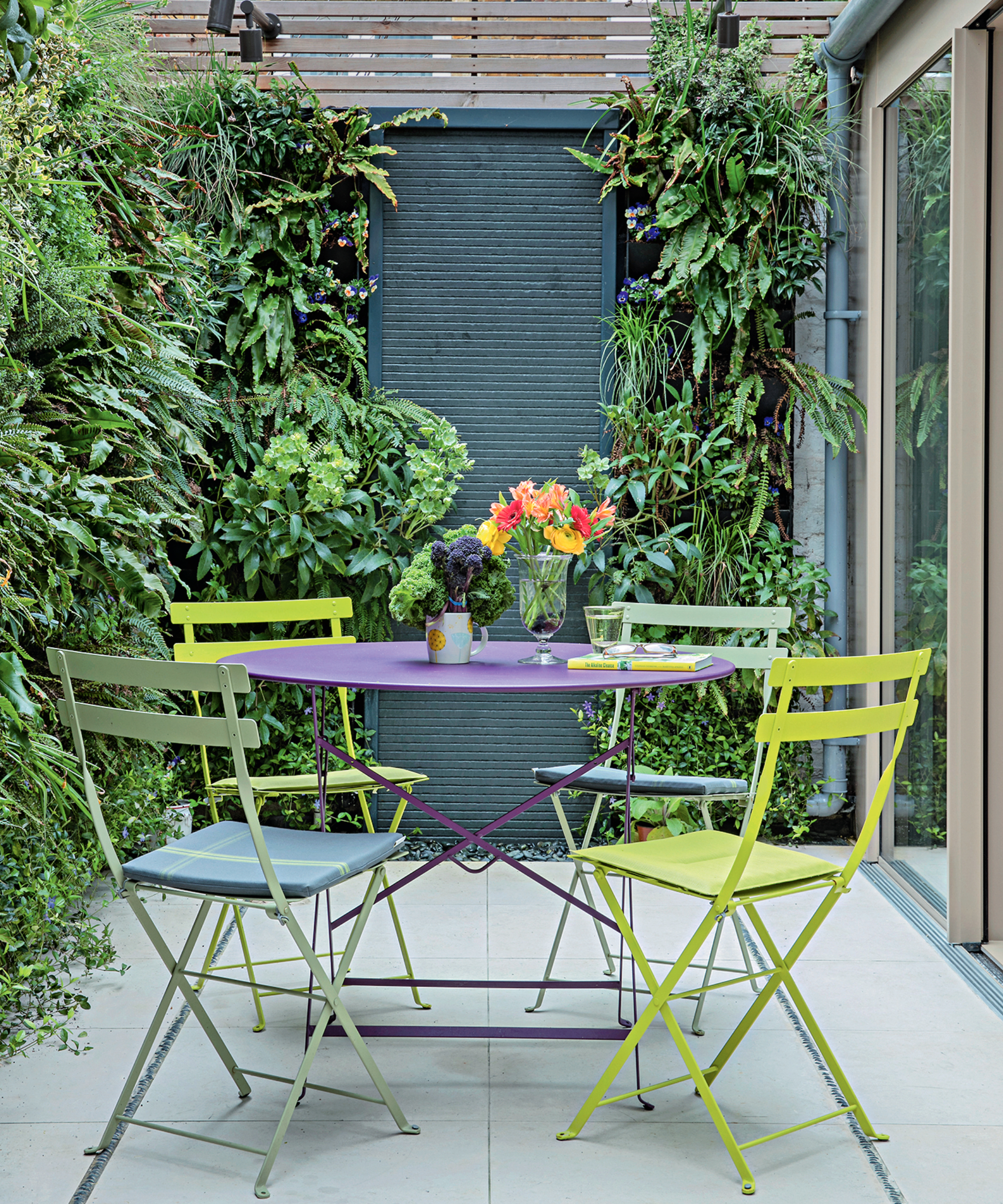 patio table and four chairs in a compact urban plot with fences painted a dark green