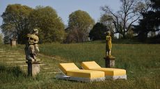 Two yellow sun loungers on a grass lawn at the bottom of a set of steps flanked by stone statues