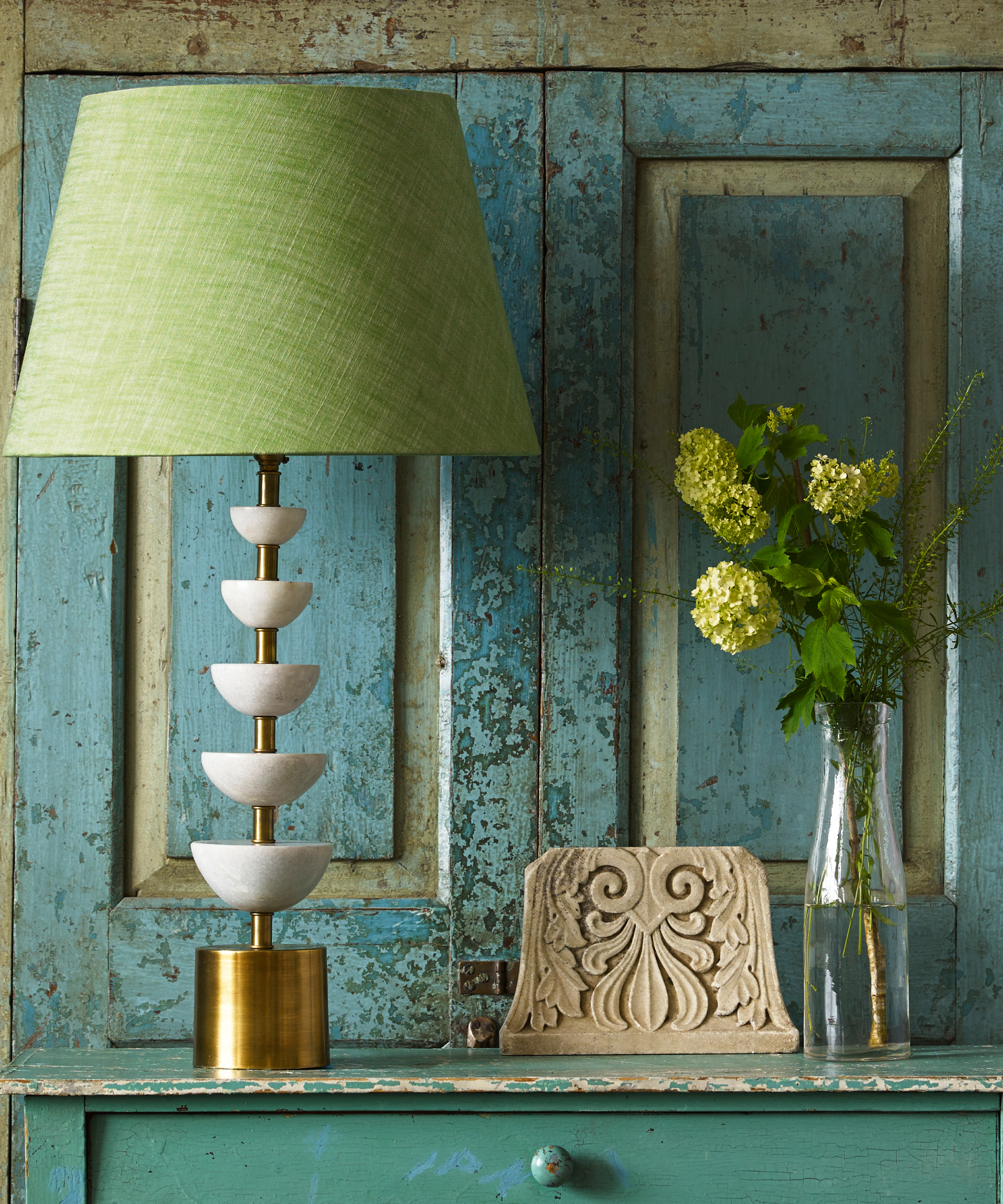 green shaded table lamp with brass and white base on green console against duck egg blue distressed wall panelling