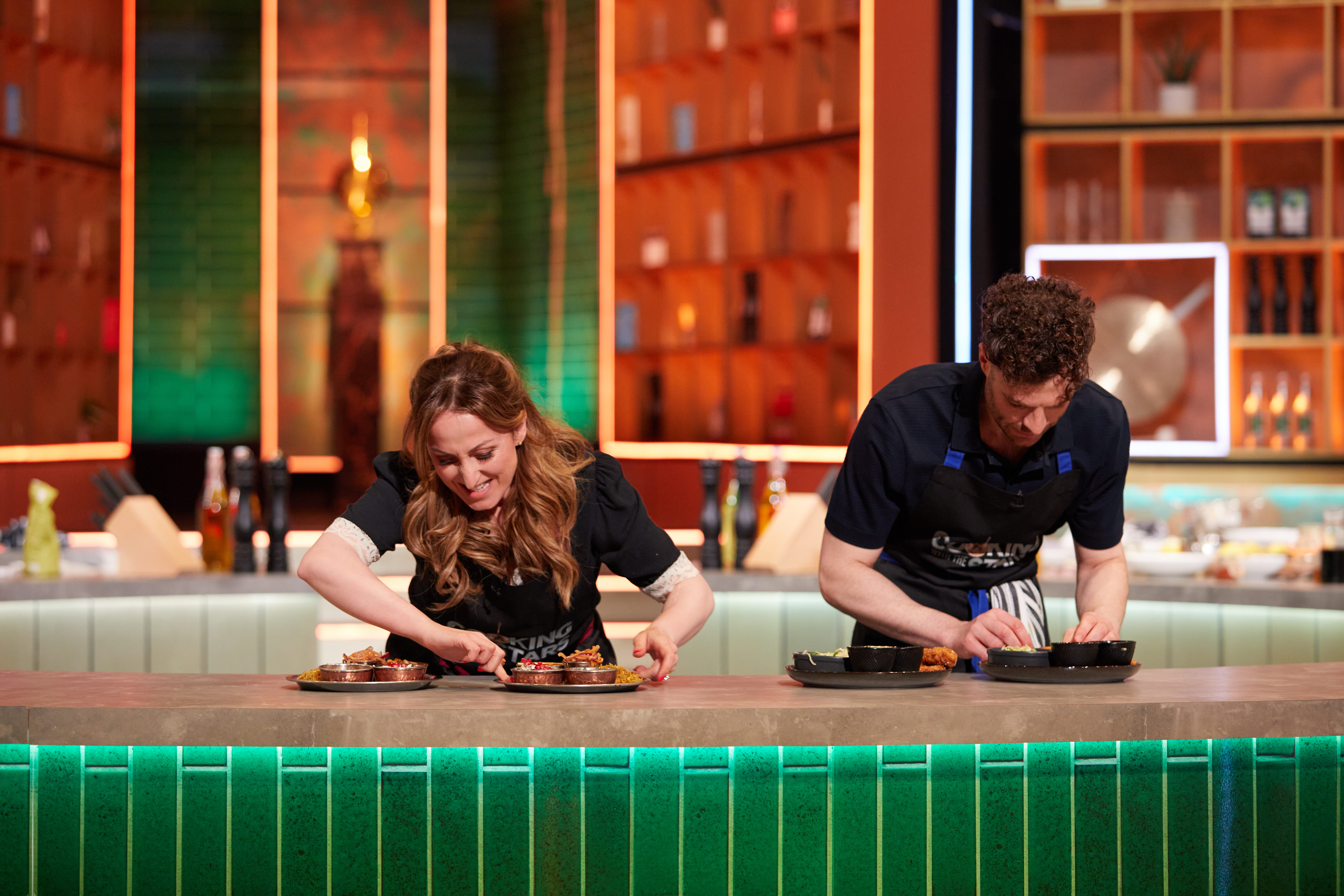Natalie Cassidy and Jordan North plate up dishes of food in the brightly lit Cooking With The Stars studio.