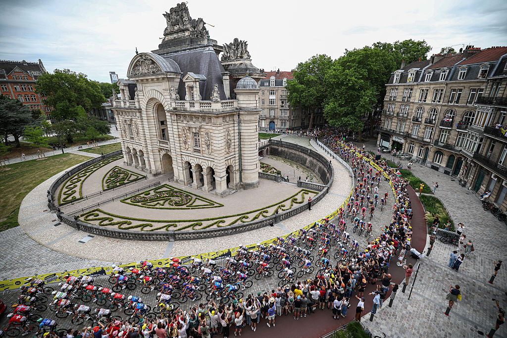 The pack of riders (peloton) cycles past the Porte de Paris arch monument near the start of the 1st stage of the 112th edition of the Tour de France cycling race, 184.9 km starting and finishing in Lille Metropole, northern France, on July 5, 2025. (Photo by Anne-Christine POUJOULAT / AFP)