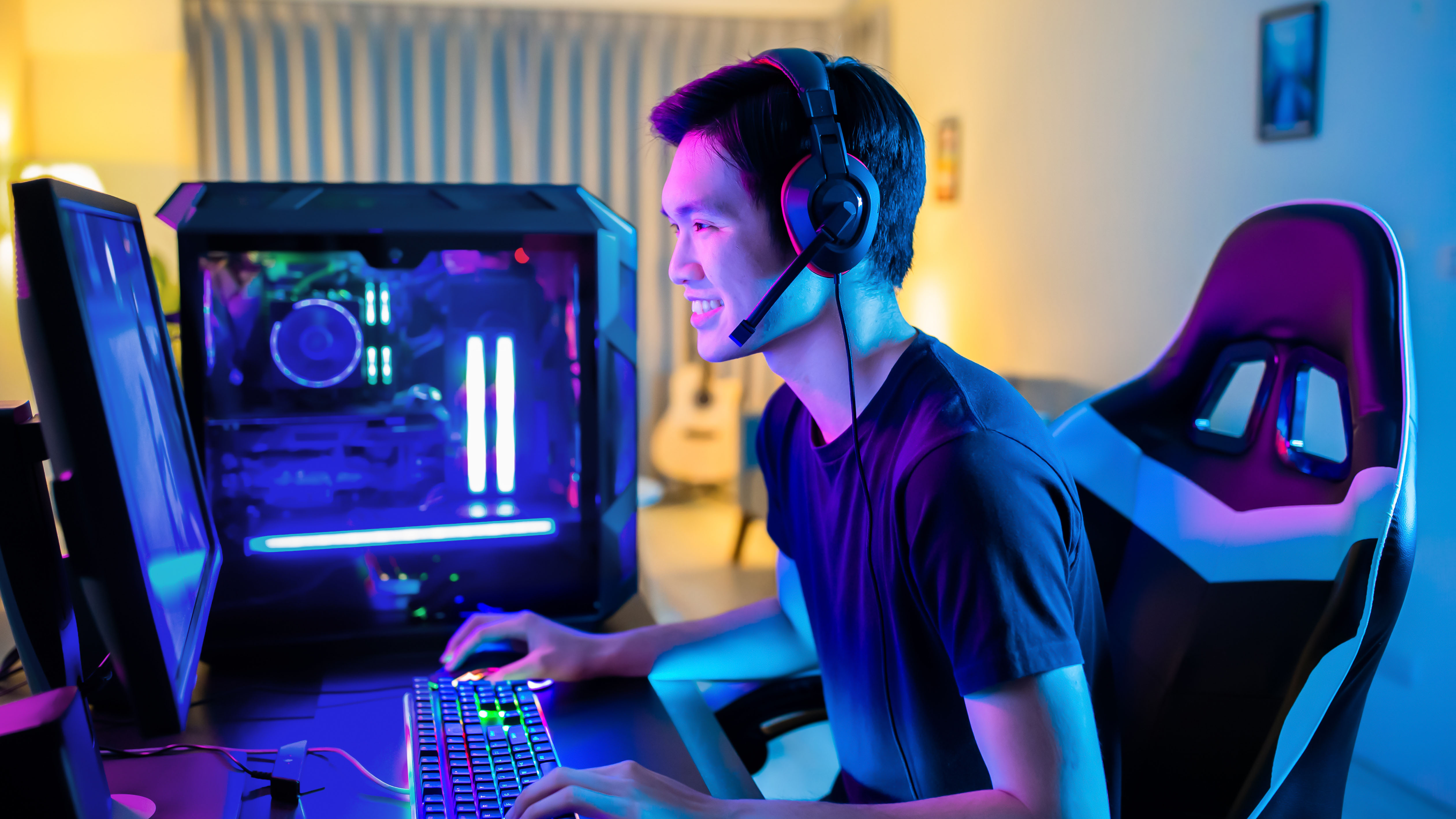 A PC gamer sitting at a desk wearing a headset with a purple-blue LED glow