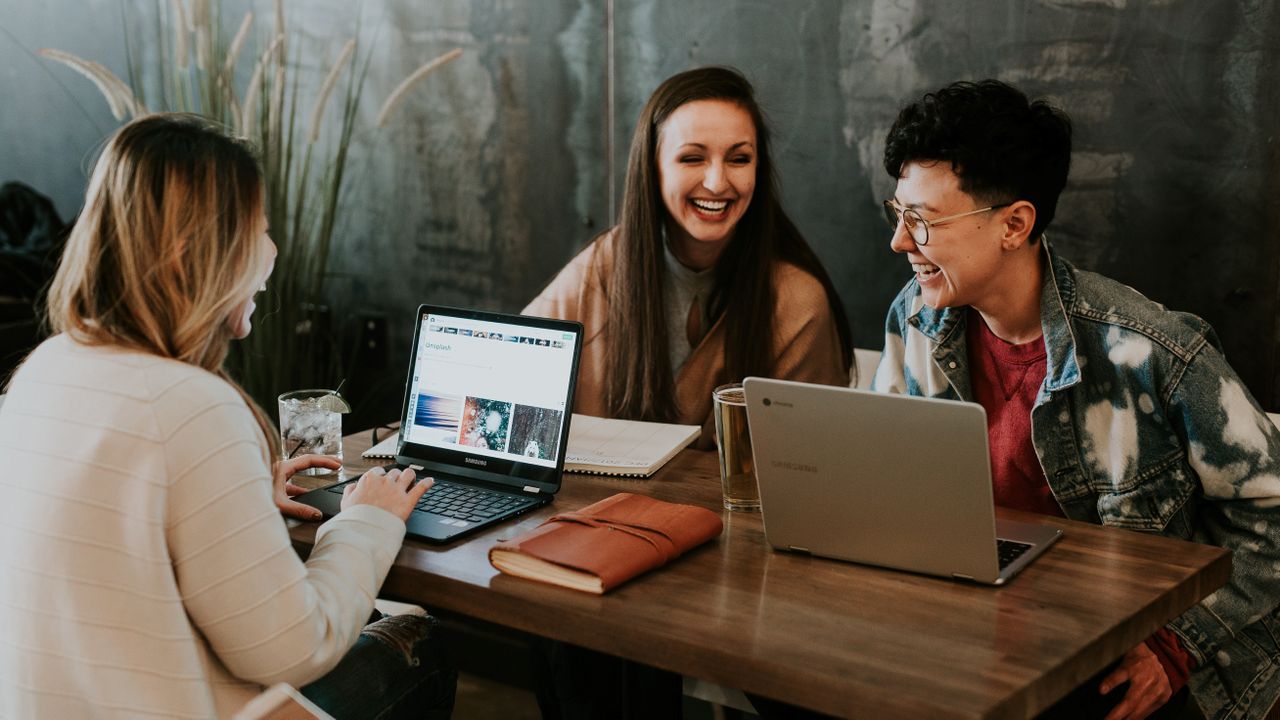 Three people sitting around table with two Chromebooks 