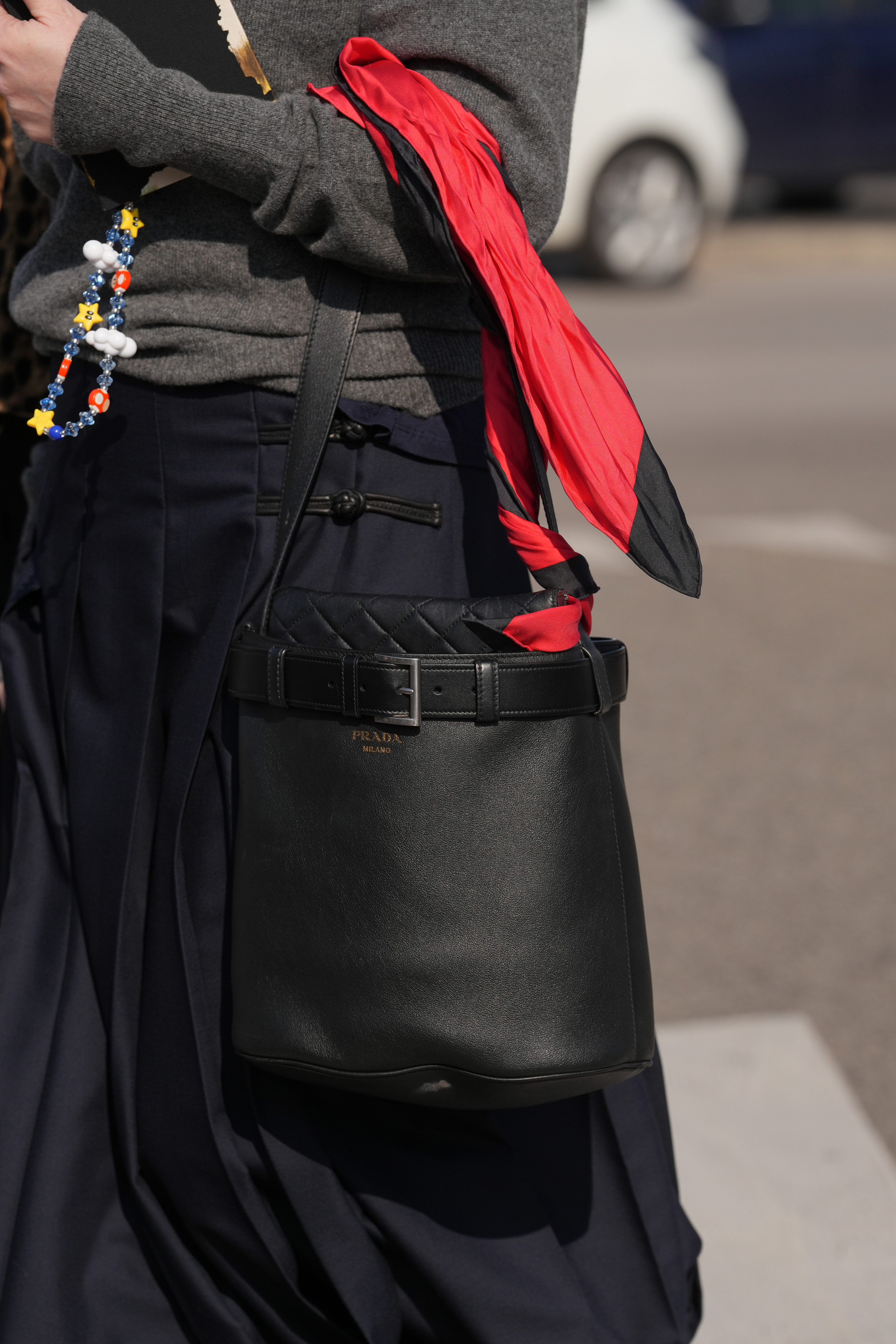 MILAN, ITALY - FEBRUARY 26: A guest is seen wearing a gray sweater, a navy skirt, a black Prada leather bucket bag, a red scarf during the Milan Fashion Week - Womenswear Fall/Winter 2026/2027 on February 26, 2026 in Milan, Italy. (Photo by Alena Zakirova/Getty Images)