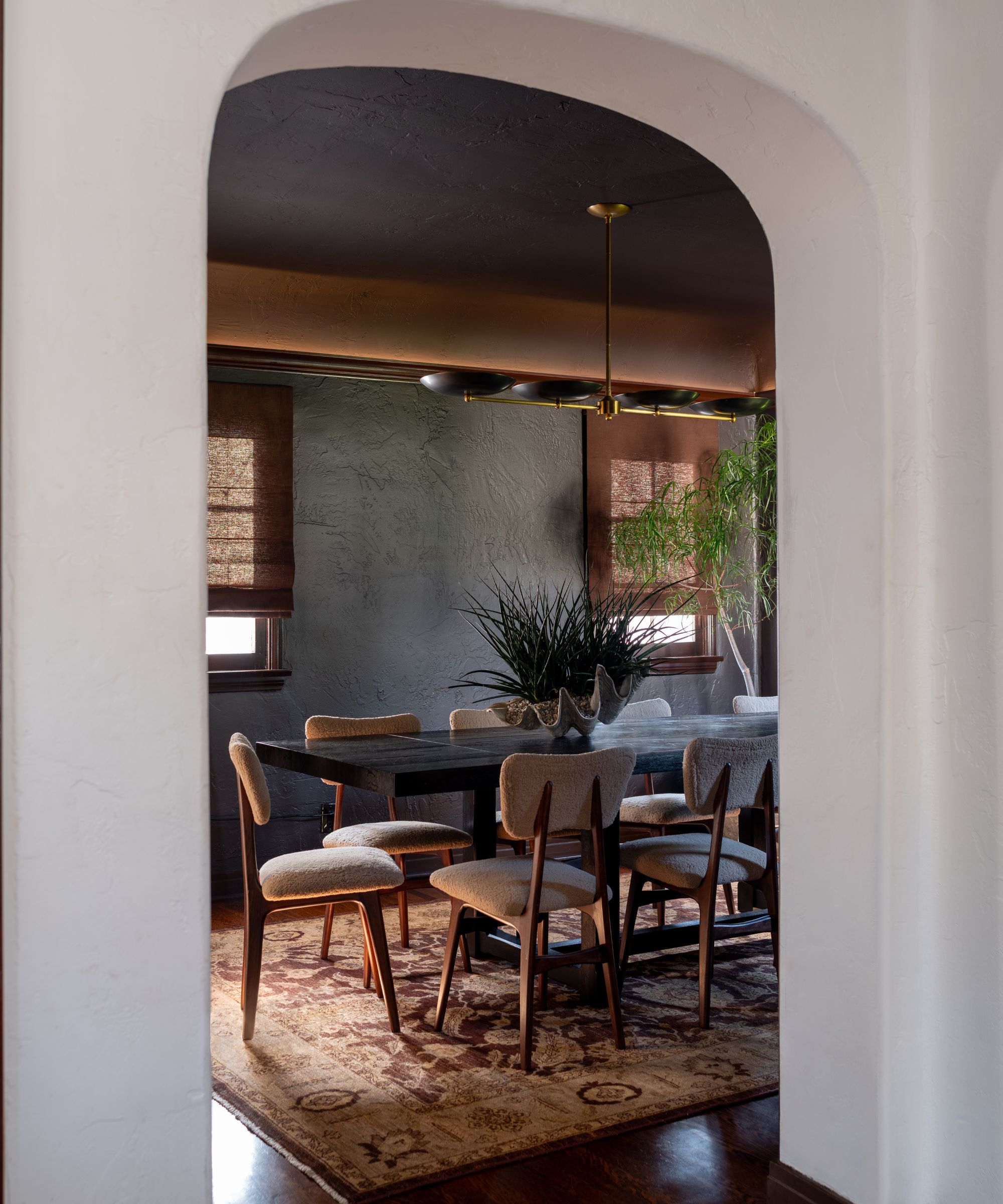 A dining room with black walls, a dark brown ceiling, and a black dining table with warm beige chairs.