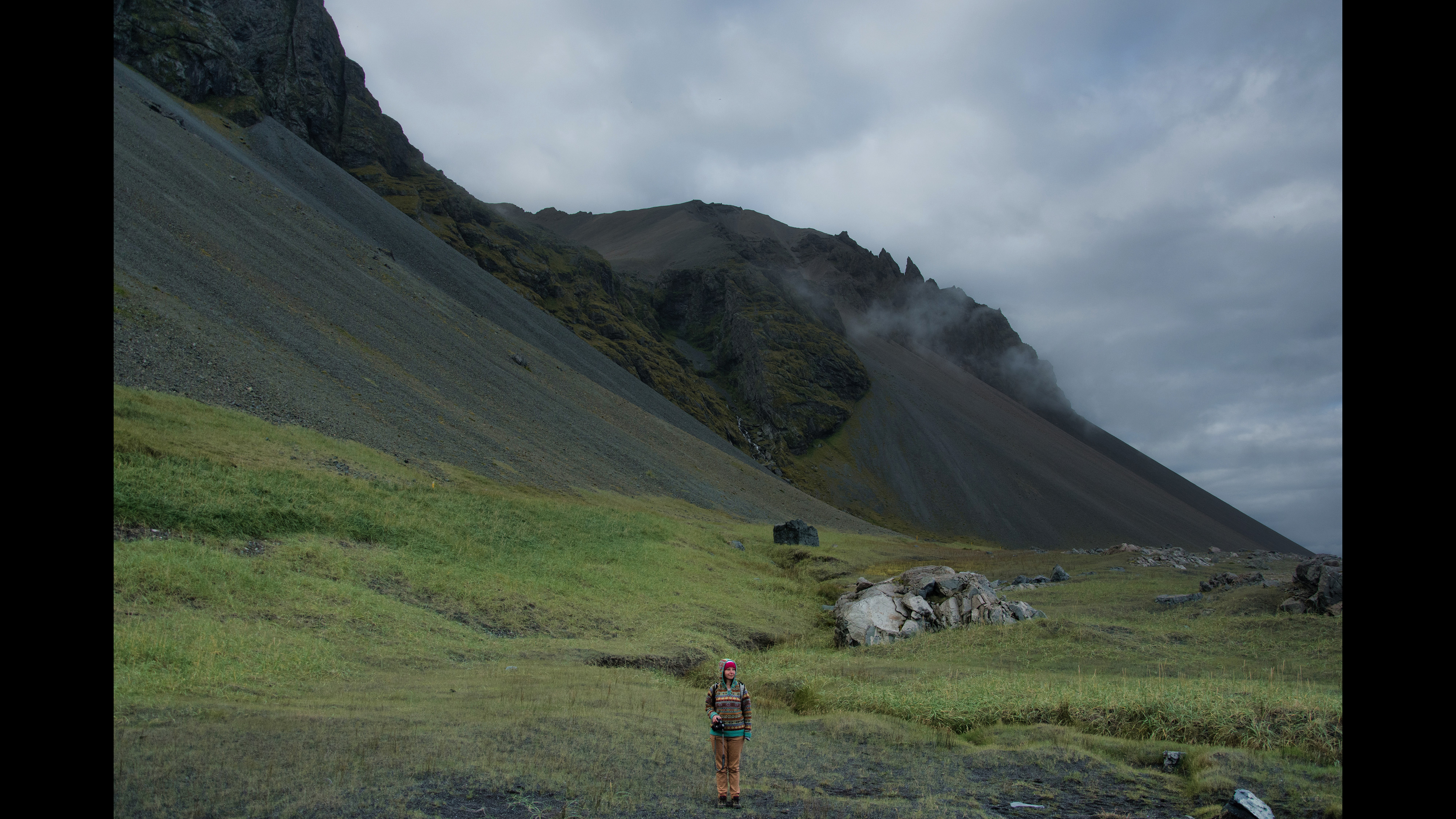 Figure in a mountainous landscape beneath a cloudy sky