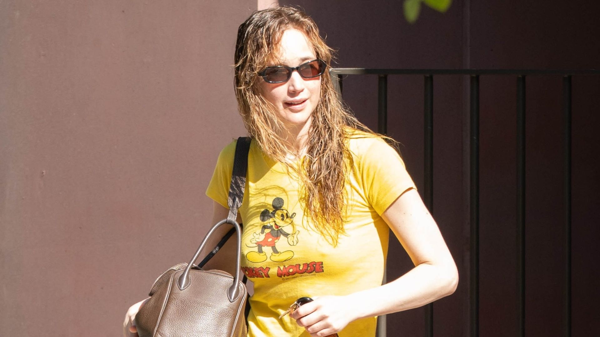 Jennifer Lawrence steps outside in New York wearing red track pants with slides and a yellow Mickey Mouse graphic tee.