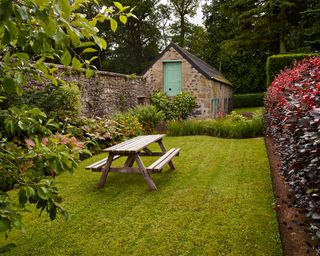 Deep flower beds by a lawn with picnic table showing how to plan a small garden planting scheme.