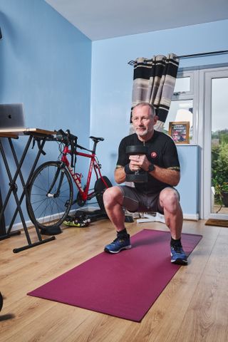 A rider in his 60s squats with a dumbell