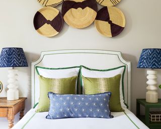 Round ceramics acting as a bedroom accent wall idea above a white and green bed with blue accessories and lampshades either side.