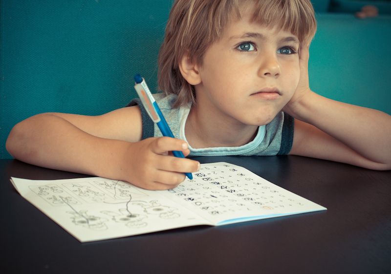 A little boy daydreams while doing his homework