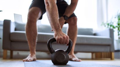 Man stands in living room as he completes a kettlebell workout