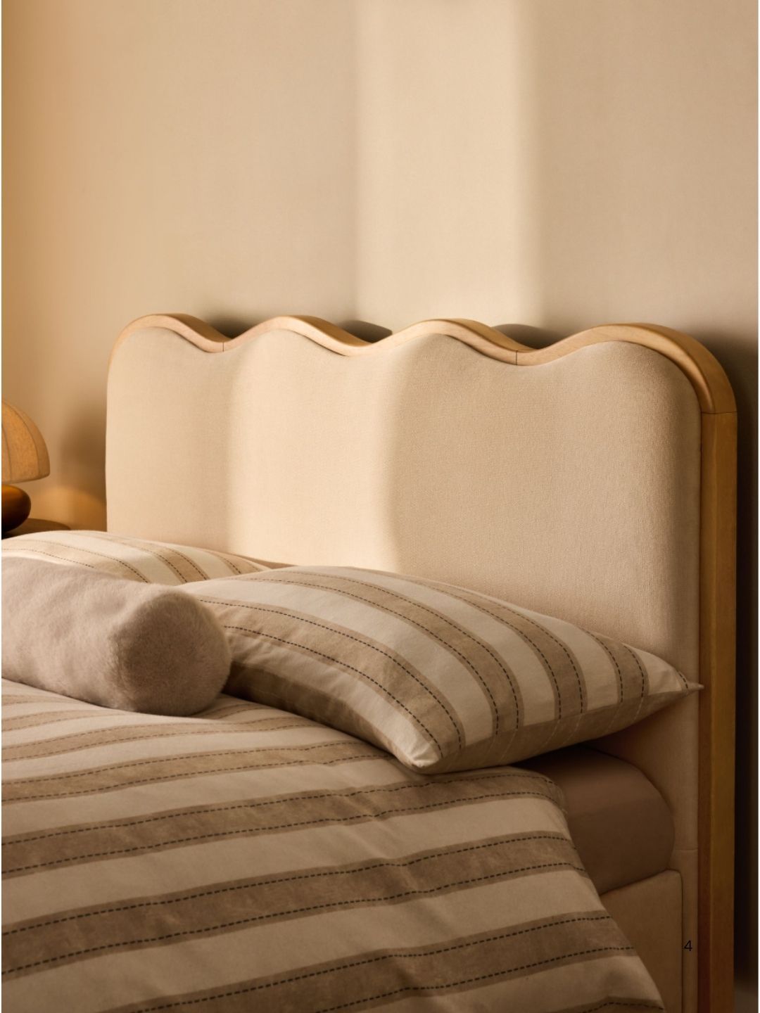 Close-up image of a wooden and upholstered scalloped bedframe with white and beige striped bedding.