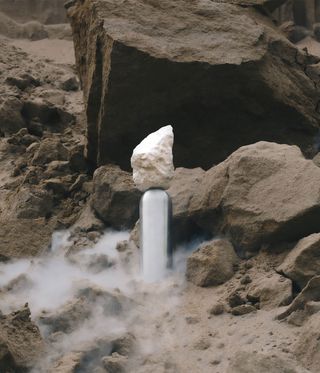 View of an aluminium and moulded concrete tabletop sculpture by Vaust pictured in front of rocks and surrounded by white smoke