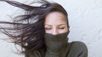 Woman wearing an olive polo neck sweater with hair blowing wildly