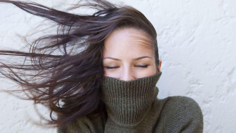 Woman wearing an olive polo neck sweater with hair blowing wildly